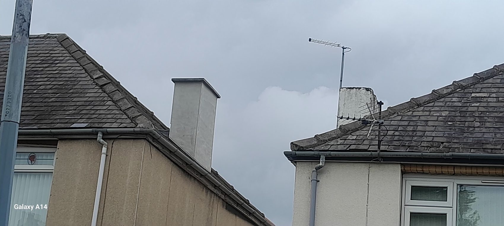 Two rooflines with a repaired chimney stack against a grey sky