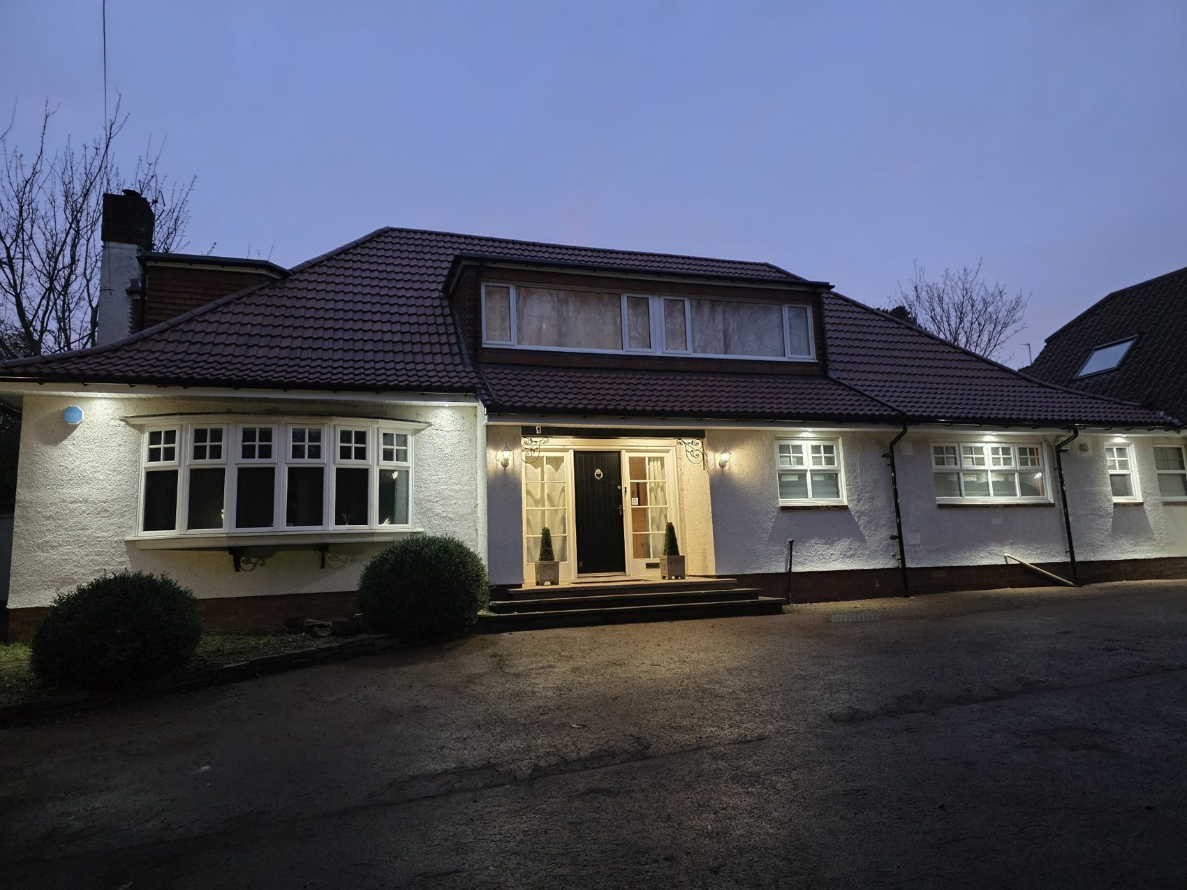 A dormer bungalow at dusk with a new dark tiled roof and lit windows