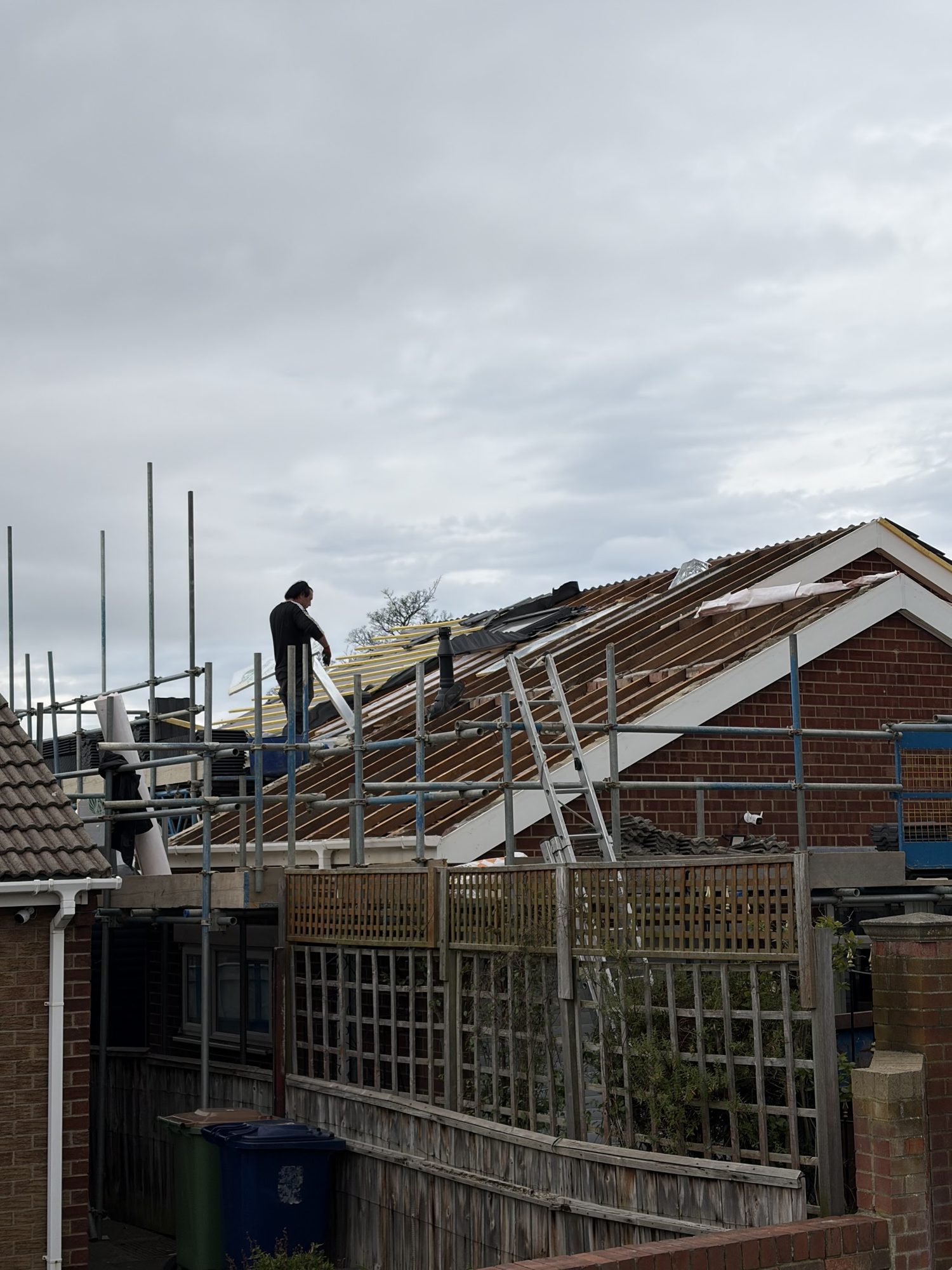 A roof stripped to the battens with scaffolding and a roofer at work